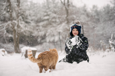 Boy tempted to throw snowball at cat stock photo