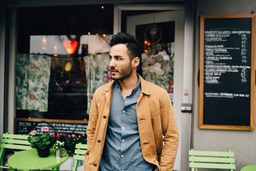 Thoughtful young man looking away while standing against restaurant - MASF10856