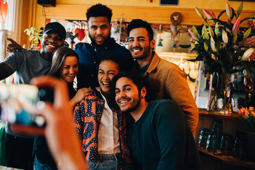 Junge Frau fotografiert fröhliche multiethnische Freunde, die beim Brunch im Restaurant stehen - MASF10861