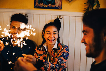Cheerful young multi-ethnic friends sitting with burning sparklers at restaurant - MASF10877