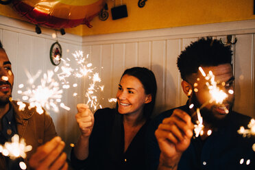 Lächelnde junge Frau mit multiethnischen männlichen Freunden, die Wunderkerzen in einem Restaurant während einer Dinnerparty halten - MASF10878