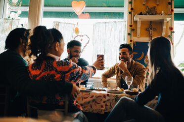 Junge Frau zeigt einem lächelnden Mann, der im Restaurant sitzt, ihr Smartphone während einer Brunchparty - MASF10884