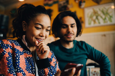 Lächelnder junger Mann und Frau teilen sich ein Smartphone, während sie in einem Restaurant beim Brunch sitzen - MASF10888