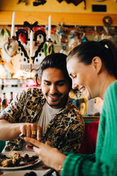 Smiling young man pointing at smart phone to woman sitting in restaurant during brunch party - MASF10894