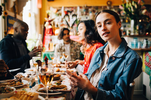 Porträt einer selbstbewussten jungen Frau, die mit ihrem Smartphone an einem Tisch im Restaurant sitzt, während einer Dinnerparty - MASF10898