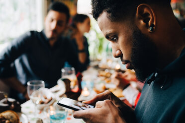 Junger Mann fotografiert das Mittagessen, während er mit Freunden in einem Restaurant auf einer Party sitzt - MASF10903