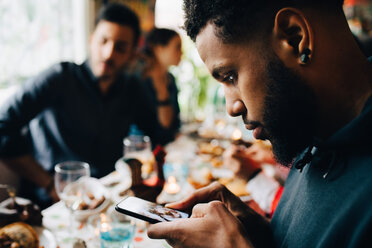 Young man photographing lunch while sitting with friends at restaurant during party - MASF10903