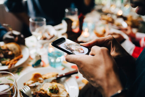 Beschnittenes Bild eines jungen Mannes, der in einem Restaurant Essen auf einem Teller fotografiert - MASF10907