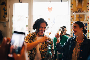 Mann fotografiert fröhliche junge Freunde, die in einem Restaurant beim Brunch einen Toast aussprechen - MASF10913