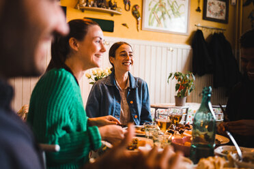 Smiling young women sitting at table in restaurant while enjoying dinner party - MASF10915