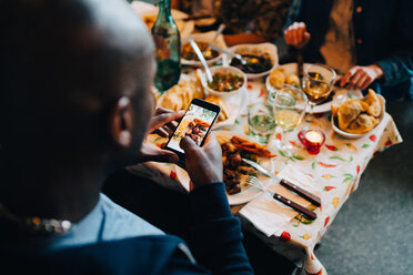 Hoher Blickwinkel eines jungen Mannes, der das Essen in einem Teller fotografiert, während er in einem Restaurant bei einer Dinnerparty sitzt - MASF10916