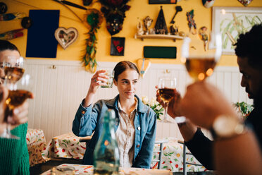 Junge Frau stößt mit multiethnischen Freunden bei einer Dinnerparty im Restaurant an - MASF10917