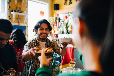 Lächelnder junger Mann, der einer Frau Essen gibt, während er mit einem Freund an einem Tisch im Restaurant während einer Brunchparty sitzt - MASF10918