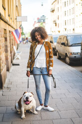 Porträt einer lächelnden erwachsenen Frau mit Hund auf dem Gehweg in der Stadt - MASF10925