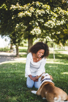 Lächelnde erwachsene Frau, die einen Stock hält, während sie mit einem Hund im Park spielt - MASF10930