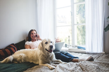 Dog resting with senior woman talking on mobile phone on bed at home - MASF10938