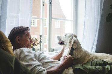 Älterer Mann liest ein Buch und entspannt sich mit seinem Hund auf dem Bett zu Hause - MASF10946