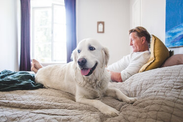 Hund, der wegschaut, während er sich mit einem älteren Haustierbesitzer auf dem Bett zu Hause entspannt - MASF10950