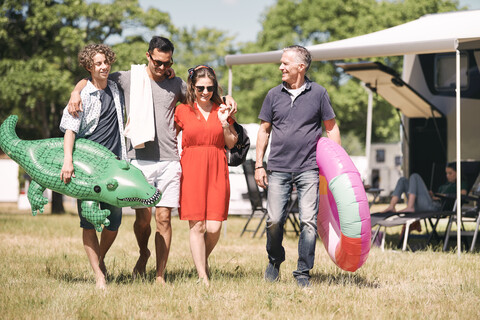 Glückliche Familie mit aufblasbaren Ringen, die auf einer Wiese neben einem Wohnwagen spazieren geht, lizenzfreies Stockfoto