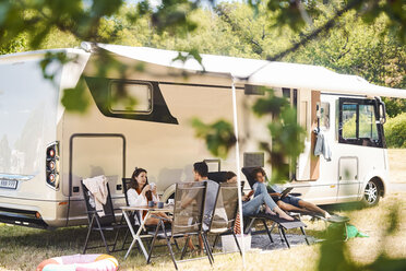 Familie entspannt sich auf Stühlen außerhalb des Wohnmobils auf dem Campingplatz während der Sommerferien - MASF10958