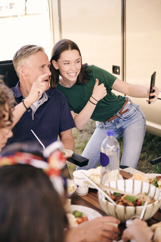 Teenager-Mädchen macht Selfie mit Großvater auf dem Handy, während sie auf dem Campingplatz isst, lizenzfreies Stockfoto