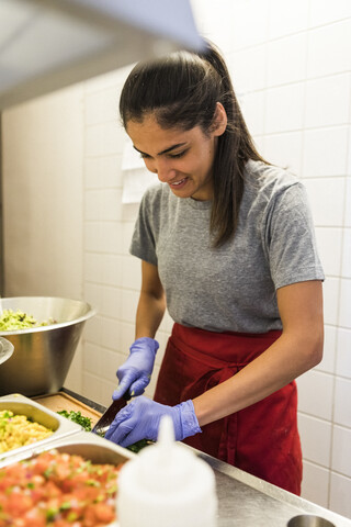 Lächelnder junger Koch, der Lebensmittel in einer Großküche eines Restaurants zerkleinert, lizenzfreies Stockfoto