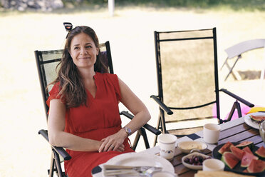 Nachdenklich lächelnde Frau sitzt am Tisch auf einem Klappstuhl auf einem Campingplatz - MASF11028