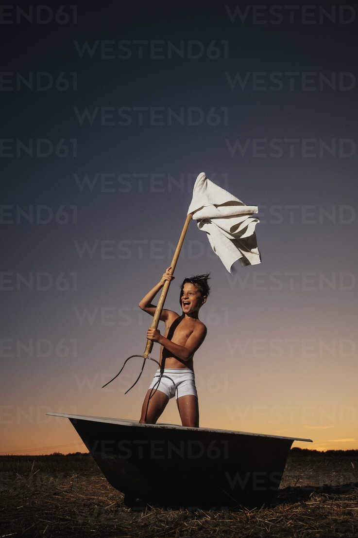 Playful boy in underwear waving pitchfork white flag in bathtub in rural  field stock photo