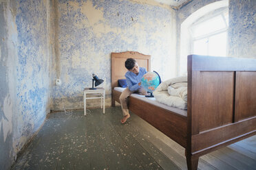 Junge schaut auf Globus auf rustikalem Bauernbett - FSIF03719