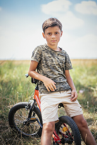 Porträt ernster Junge auf Fahrrad in Feld, lizenzfreies Stockfoto