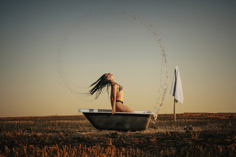 Frau im Bikini, die ihre Haare in einer Badewanne in einem ländlichen Gebiet spritzt, lizenzfreies Stockfoto
