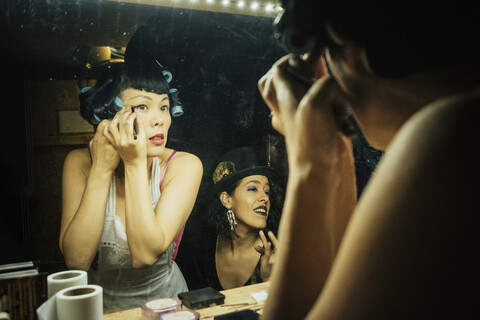 Burlesque-Darstellerinnen machen sich bereit und schminken sich vor dem Spiegel in der Garderobe, lizenzfreies Stockfoto