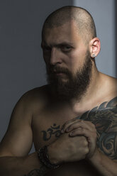 Portrait tough man with beard and tattooed chest, making fist - FSIF03765
