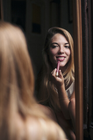 Spiegelbild einer lächelnden jungen Frau, die Lippenstift aufträgt, lizenzfreies Stockfoto