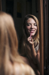 Spiegelbild einer lächelnden jungen Frau, die Lippenstift aufträgt - LOTF00056