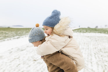 Boy carrying happy sister piggyback in winter landscape - KMKF00684