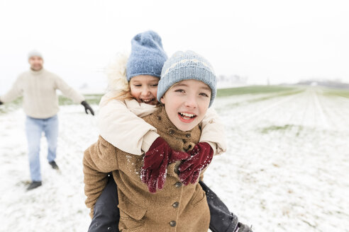 Junge trägt glückliche Schwester huckepack in Winterlandschaft - KMKF00685