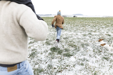 Vater, Sohn und Hund laufen auf einem verschneiten Feld im Winter - KMKF00691