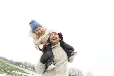 Playful father carrying daughter piggyback in winter landscape - KMKF00699