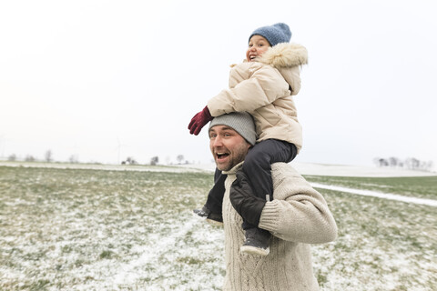 Playful father carrying daughter piggyback in winter landscape stock photo