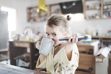 Porträt eines kleinen Mädchens mit Smartphone beim Teetrinken in der Küche - KMKF00714