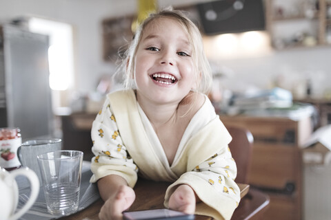 Porträt eines glücklichen kleinen Mädchens mit Smartphone in der Küche, lizenzfreies Stockfoto