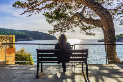 Spain, Mallorca, Sant Elm, woman sitting on bench, rear view stock photo