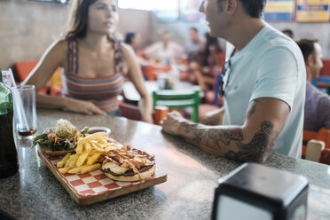 Hamburger and French fries on counter in a bar with couple socializing in background - ABAF02234