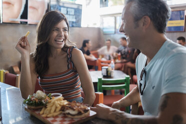 Happy couple sharing hamburger and French fries in a bar - ABAF02235