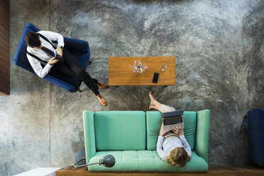 Blick von oben auf Geschäftskollegen, die mit Laptop und Smartphone in einem Coworking Space arbeiten - SBOF01546