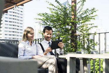 Smiling business colleagues on city terrace looking at tablet - SBOF01549
