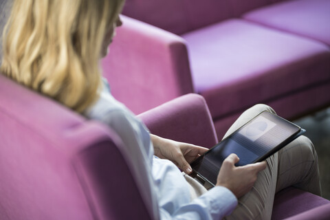 Geschäftsfrau auf violettem Sessel sitzend mit Tablet, lizenzfreies Stockfoto