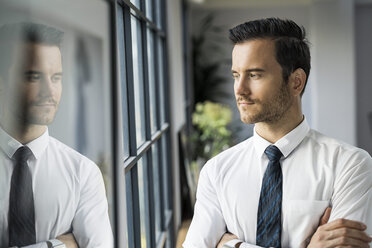 Confident businessman in office looking out of window - SBOF01566