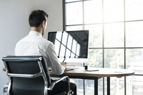 Geschäftsmann im Büro arbeitet am Computer vor dem Fenster - SBOF01572